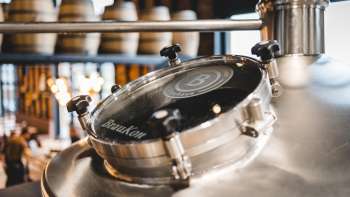 Primo piano di una finestra di visualizzazione rotonda su un bollitore lucido con una vista della sala di produzione della birra sullo sfondo.