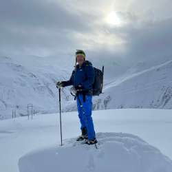 Nikolaus Büchel in piedi con zaino e bastoncini durante un'escursione con le racchette da neve in un paesaggio invernale di alta montagna