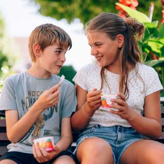Due bambini siedono su una panchina del parco in Liechtenstein e mangiano un gelato - volti sorridenti, fiori e un'atmosfera estiva in campagna