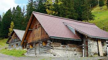 Storico edificio in legno del vecchio centro giovanile di Malbun di fronte a un pendio boscoso.
