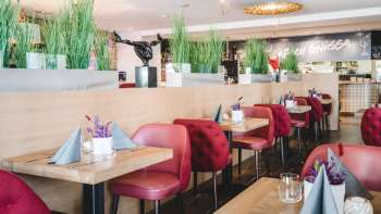 : Tavoli generosamente disposti nel PUR Restaurant & Bar con sedie rosse e decorazioni floreali.