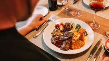 Primo piano di un piatto principale con carne, verdure e salse pregiate, accompagnato da vino rosso