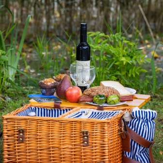 Cestino da picnic con specialità regionali, pane fresco, frutta e vino, disposti con cura in un prato immerso nella natura.