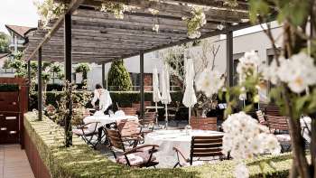Un'elegante terrazza con tavoli bianchi apparecchiati con tovaglioli e bicchieri sotto un padiglione di legno, circondato da una vegetazione lussureggiante. Un'elegante terrazza con tavoli bianchi apparecchiati con tovaglioli e bicchieri sotto un padiglione di legno, circondato da una vegetazione lussureggiante.