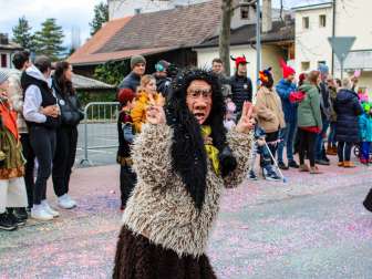 Strega di Schaan mascherata alla sfilata di carnevale di Schaan, davanti a un pubblico e a coriandoli colorati sulla strada