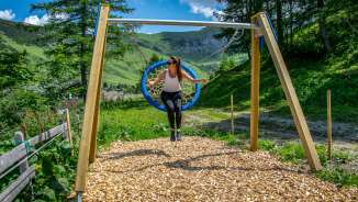 Donna che si dondola su un'altalena a nido a Malbun, Liechtenstein, circondata da montagne, prati e natura estiva