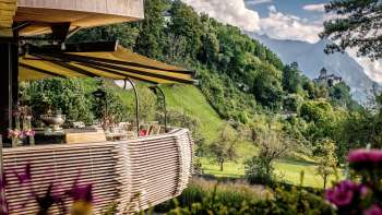 Terrazza soleggiata con fiori in fiore e tavoli elegantemente apparecchiati con vista sulla valle