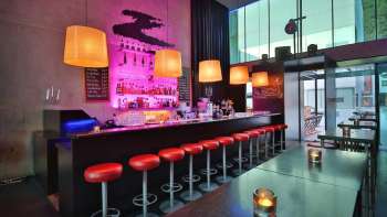 Bar moderno con banconi lunghi, sgabelli rossi e illuminazione elegante in rosa e arancione