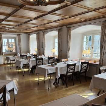 Sala da pranzo luminosa e classica con tovaglie bianche e pavimento in legno.