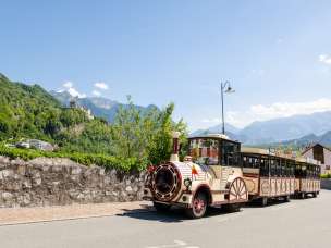 Trenino turistico che attraversa Vaduz, sullo sfondo il castello di Vaduz e le Alpi in pieno sole