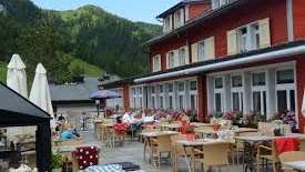 Terrazza soleggiata del ristorante con tavoli coperti, ombrelloni e vista sulle Alpi.