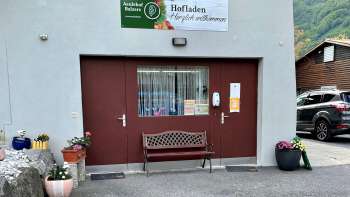 Ingresso del negozio della fattoria Aeulehof con cancello rosso, panchina e decorazioni floreali a Triesen, Liechtenstein.