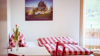 Accogliente camera doppia nella guest house del Camping Mittagsspitze con lenzuola e decorazioni a scacchi rossi e bianchi.