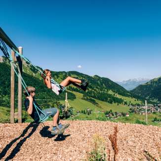 Due bambini che si dondolano in un parco giochi di montagna con vista sul panorama estivo di Malbun in Liechtenstein