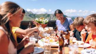 Famiglia che pranza insieme su una terrazza soleggiata a Sarreis, circondata da montagne e specialità regionali
