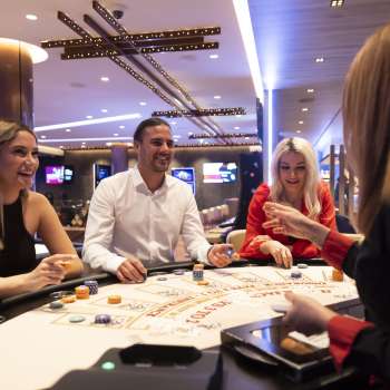 Atmosfera amichevole al tavolo da gioco: tre ospiti chiacchierano con il croupière nel Casinò Schaanwald, arredato con stile.