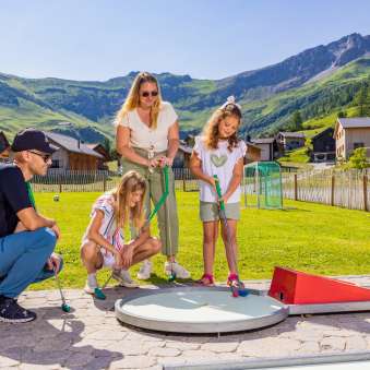 Famiglie che giocano insieme a minigolf nel soleggiato villaggio di montagna di Malbun, in Liechtenstein: divertimento per grandi e piccini sulle Alpi.