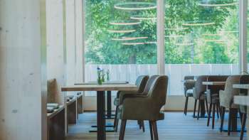 Ristorante luminoso e moderno con rivestimenti in legno, comodi posti a sedere e grandi finestre con vista sul verde