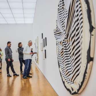 I visitatori ammirano le opere d'arte moderna in una galleria del Kunstmuseum Liechtenstein con architettura chiara e pavimento in legno