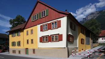 Landweibels-Huus tradizionale con facciata gialla e rossa sullo sfondo delle montagne del Liechtenstein.