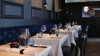 Eleganti interni dell'Esquire Bar & Bistro di Vaduz con tavoli apparecchiati con stile, panche imbottite blu scuro e illuminazione d'atmosfera.