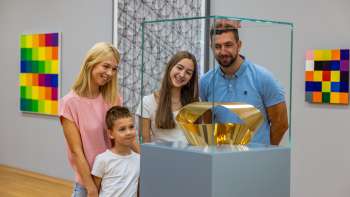 Famiglia con due bambini che osserva una vetrina con una scultura d'oro nel museo
