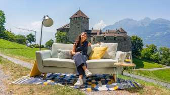 Donna seduta su un divano con vista sul castello di Vaduz e le montagne del Liechtenstein, ambiente moderno all'aperto con decorazioni
