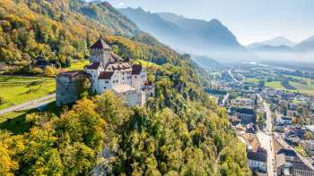 Vista del castello di Vaduz con la foresta dai colori autunnali e la città di Vaduz nella valle.