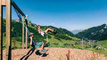 Due bambini che si dondolano con vista su Malbun