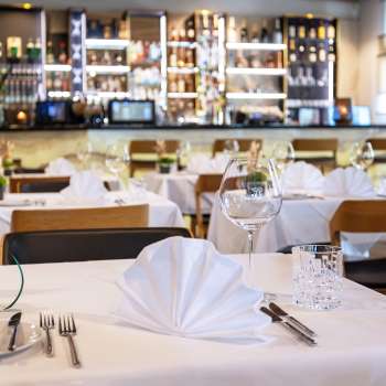  Tavola apparecchiata con gusto nel ristorante Alpspitz con vista sul bar sullo sfondo.