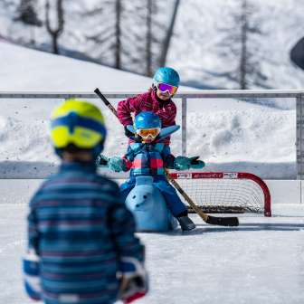 Bambini giocano con caschi e bastoni da hockey sulla pista di ghiaccio di Malbun, un bambino si siede su un aiutante di pattinaggio davanti a una porta