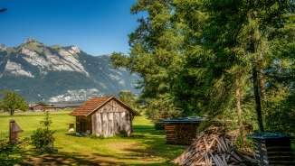 Piccolo fienile in legno su un prato con una catasta di legna da ardere e vista sulle Alpi lungo la Route 66 in Liechtenstein