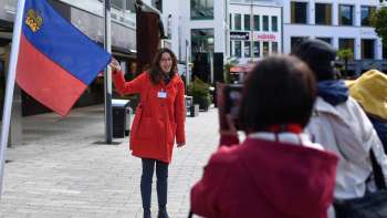 Una guida cittadina con la bandiera del Liechtenstein accoglie un gruppo di turisti a Vaduz