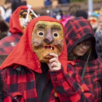 Partecipanti con maschere di legno intagliato e costumi rossi e neri alla sfilata di carnevale di Malbun