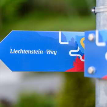 Cartello blu con la scritta «Sentiero del Liechtenstein» in un design moderno.