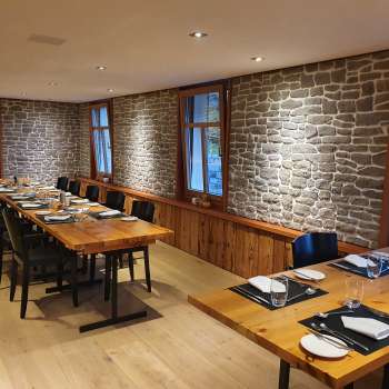 Elegante sala da pranzo con lunghi tavoli in legno, pareti in pietra e decorazioni moderne