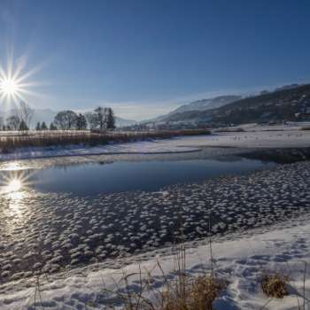 Alba sul lago Egelsee a Mauren in inverno, con ghiaccio scintillante, neve e uno sfondo di montagne soleggiate.