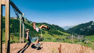 Due bambini che si dondolano in un parco giochi di montagna con vista sul panorama estivo di Malbun in Liechtenstein