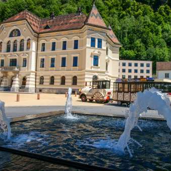 Vista del palazzo del governo di Vaduz con il trenino turistico e le fontane in primo piano