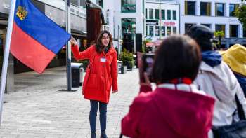 Una guida cittadina con la bandiera del Liechtenstein accoglie un gruppo di turisti a Vaduz