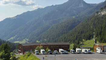 Diversi camper sono parcheggiati nella soleggiata piazzola di Malbun con un panorama montano sullo sfondo