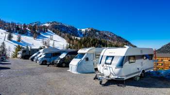 Diversi camper sono parcheggiati nella soleggiata piazzola di Malbun con un panorama montano sullo sfondo