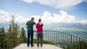 Due persone si godono la vista dal punto panoramico di Gaflei sulla valle del Reno nel Liechtenstein in una giornata limpida.