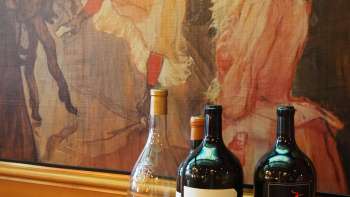Tre bottiglie di vino davanti a un murale artistico nella Brasserie Burg: l'eleganza mediterranea incontra l'estro artistico.