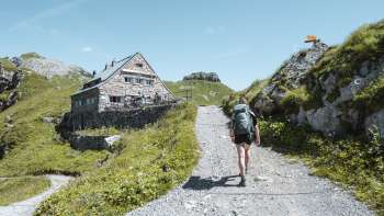 Escursionista con zaino che cammina lungo un sentiero di montagna verso il rifugio Pfälzerhütte nelle Alpi del Liechtenstein.