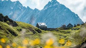 Vista del rifugio Pfälzerhütte, situato su un verde pascolo alpino di fronte a ripide pareti rocciose nelle Alpi del Liechtenstein.