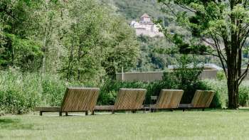 Tranquillo prato per prendere il sole con lettini in legno nel Parco Naturale di Haberfeld, con vista sul castello sullo sfondo.