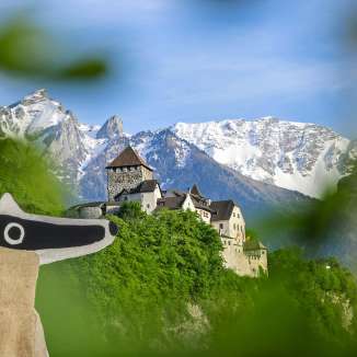 Veduta del castello di Vaduz con la percorso dei detective in primo piano e le Alpi innevate sullo sfondo.