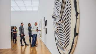 I visitatori ammirano le opere d'arte moderna in una galleria del museo d’arte del Liechtenstein con architettura chiara e pavimento in legno