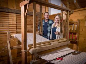 Una coppia osserva un telaio storico funzionante nel Museo Walser di Triesenberg, in Liechtenstein, circondato da pannelli in legno.